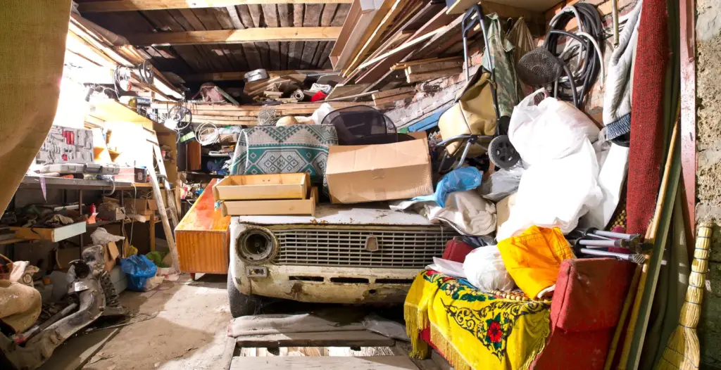 Altes Auto unter Ger&uuml;mpel in einer vollgestellten Garage.