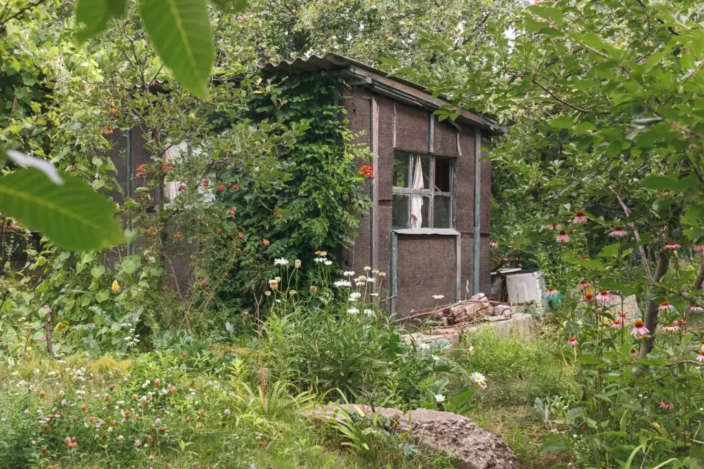 Zugewachsene Gartenlaube zwischen Blumen und Obstb&auml;umen.