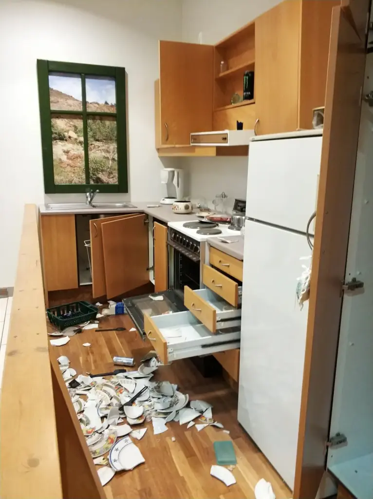 Verw&uuml;stete K&uuml;che mit zerbrochenem Geschirr und offenen Schubladen.