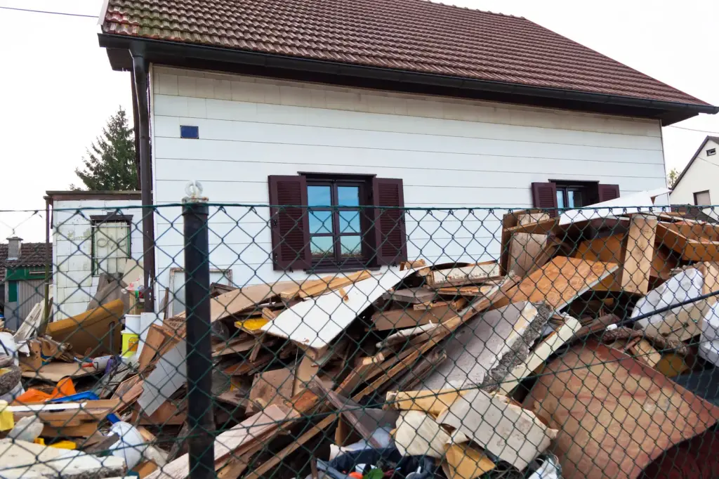 Sperrm&uuml;ll- und Schutthaufen hinter einem Zaun vor einem Wohnhaus.
