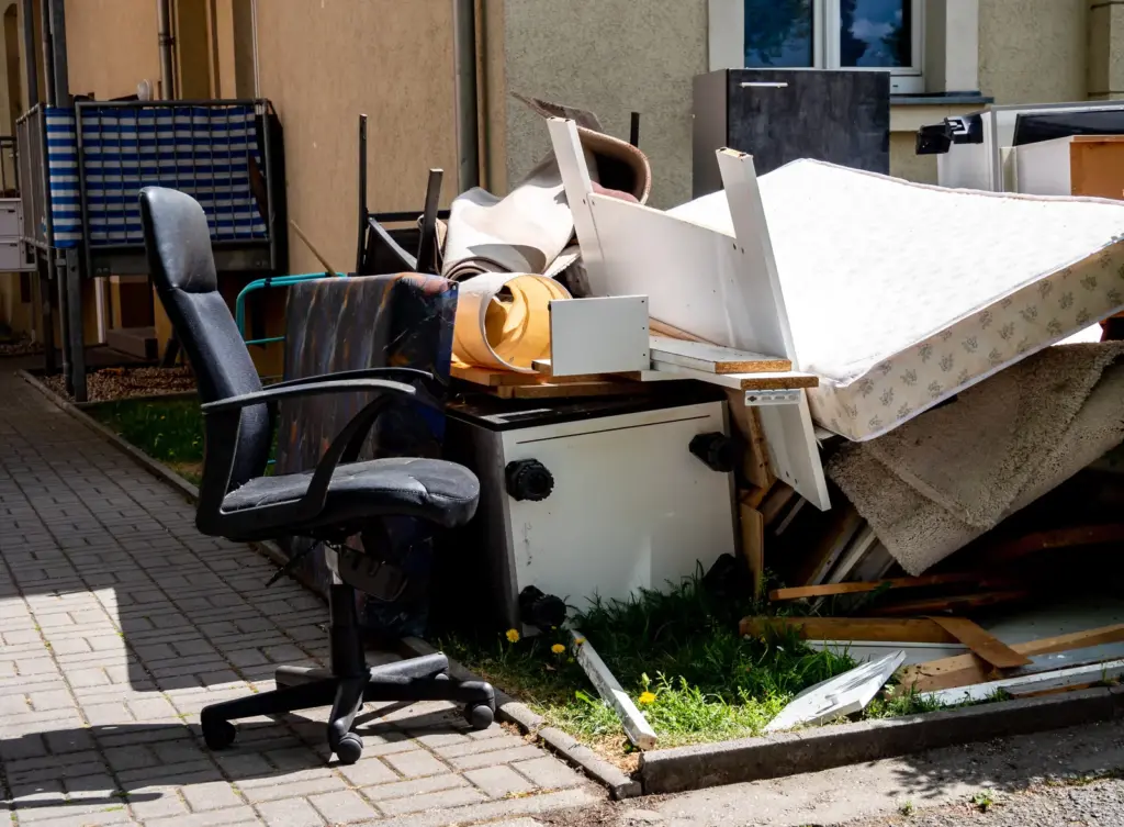 B&uuml;rostuhl vor Sperrm&uuml;llhaufen mit Matratze und M&ouml;belteilen.
