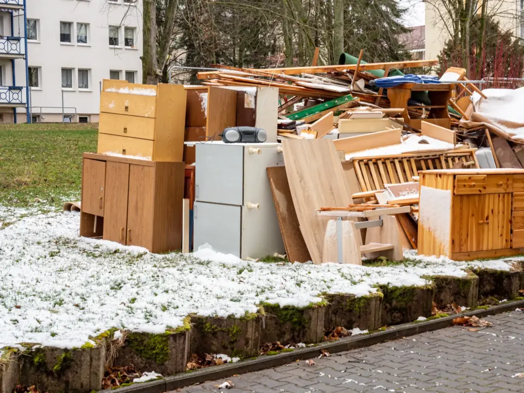 Sperrm&uuml;ll mit Schr&auml;nken und Holzlatten im Schnee vor einem Wohnblock.