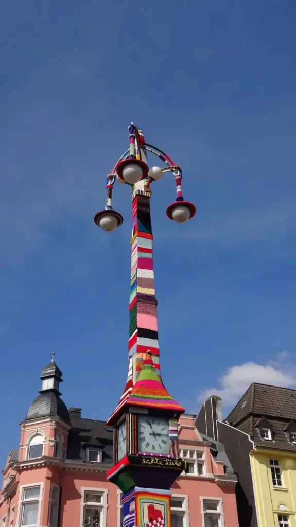 Mit bunten Strickarbeiten umh&uuml;llte historische Uhrens&auml;ule in Dortmund-H&ouml;rde.