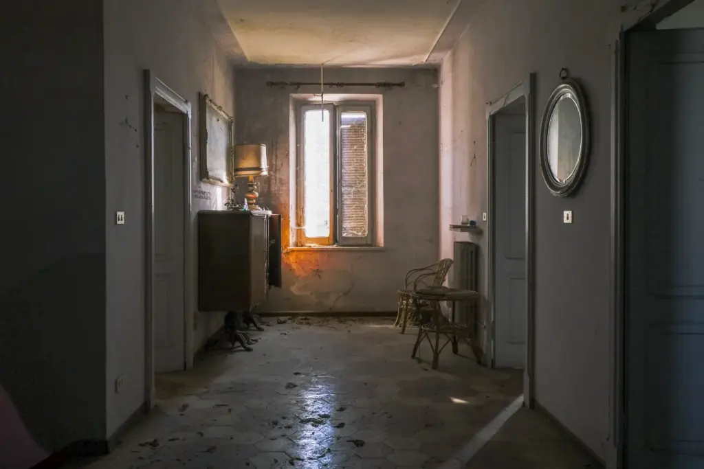 Flur einer alten Wohnung mit Kommode, Spiegel und Korbstuhl.